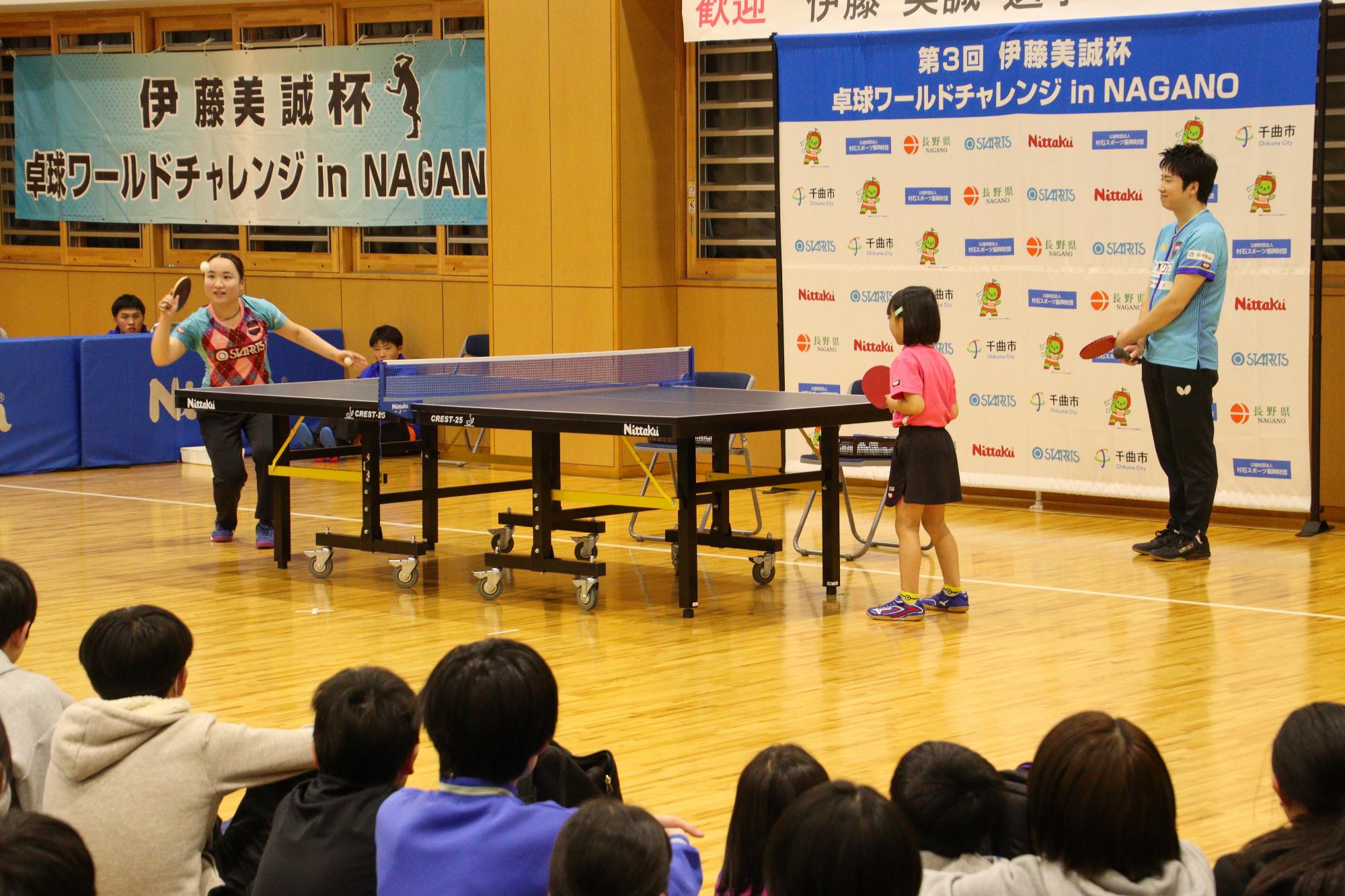 卓球交流イベントで伊藤選手にサーブを教わっている参加者とそれを見守る水谷さん